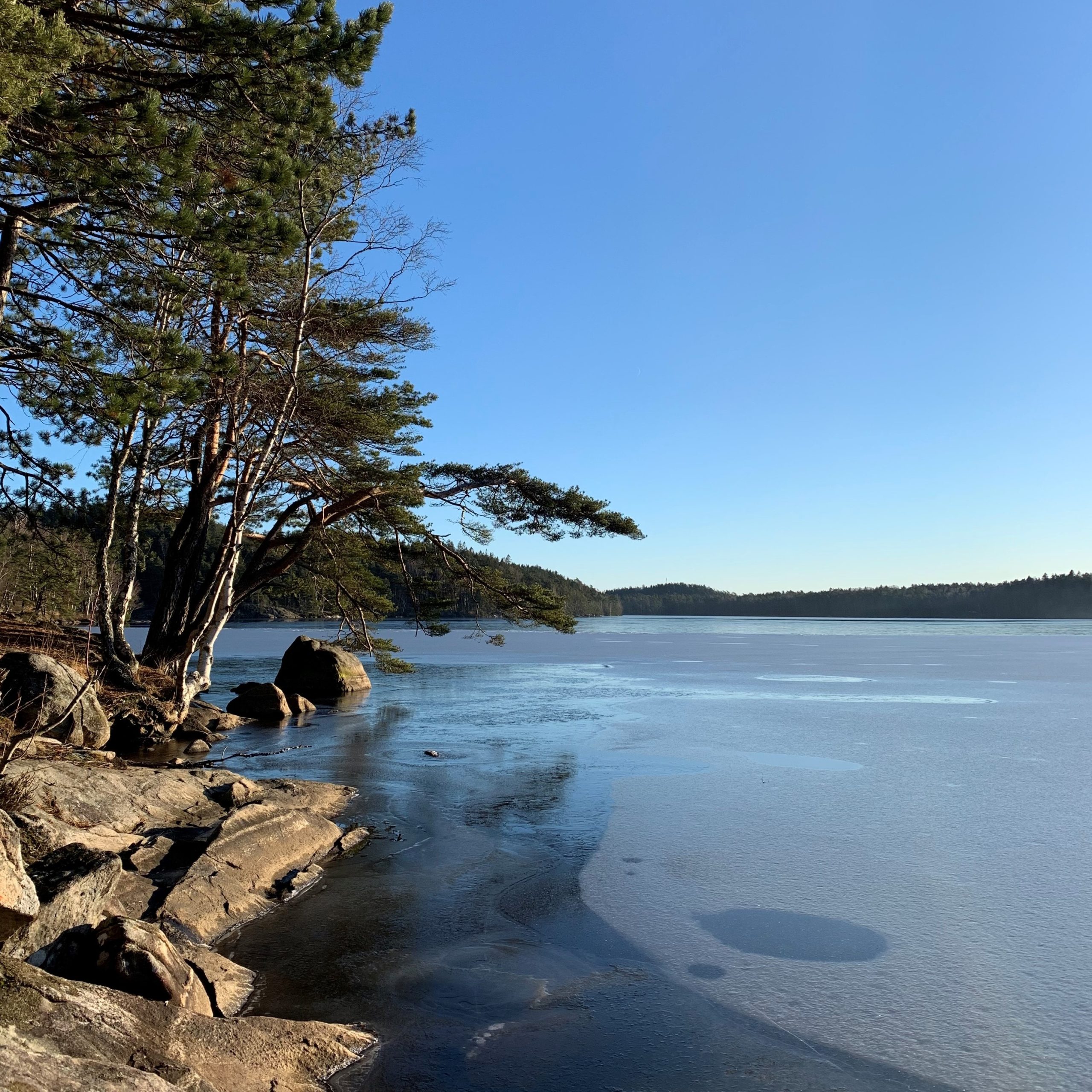 soliga klippor intill en frusen sjö och blå himmel