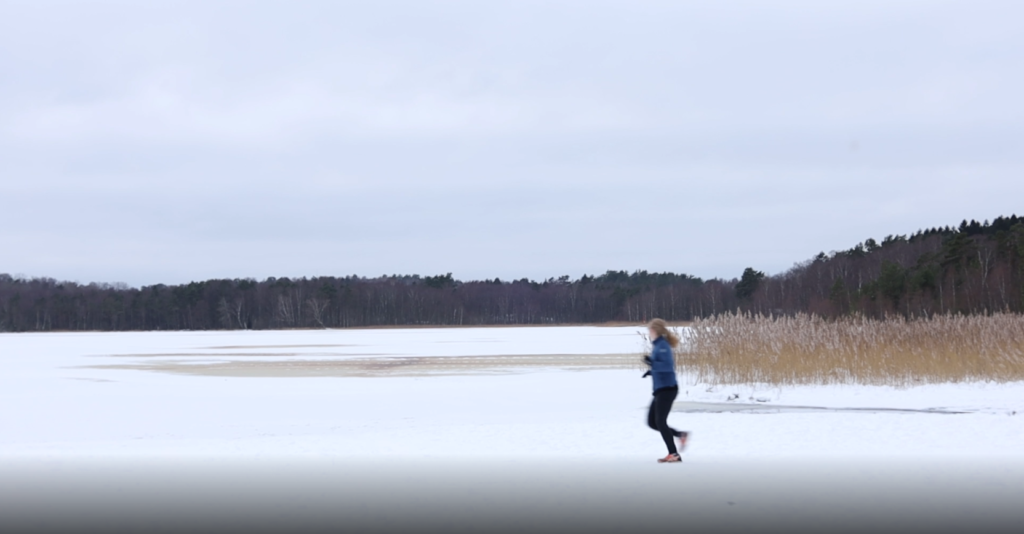 Kvinnlig motionär i Skatås på vintern, framför frusen sjö. Skog syns bakgrunden.